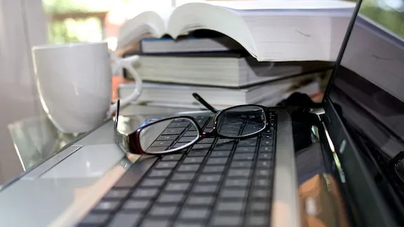 Glasses on a laptop. Pile of books and a cup in the back.