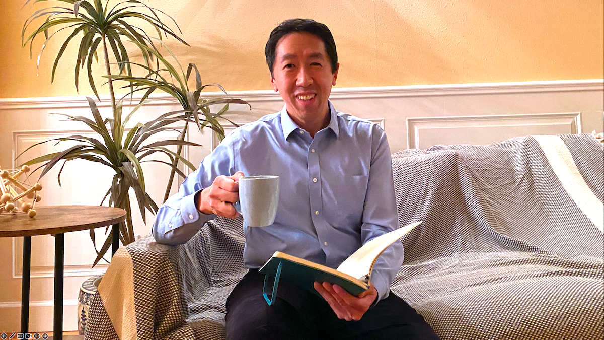 Andrew Ng on a couch with a cup of coffee and a book