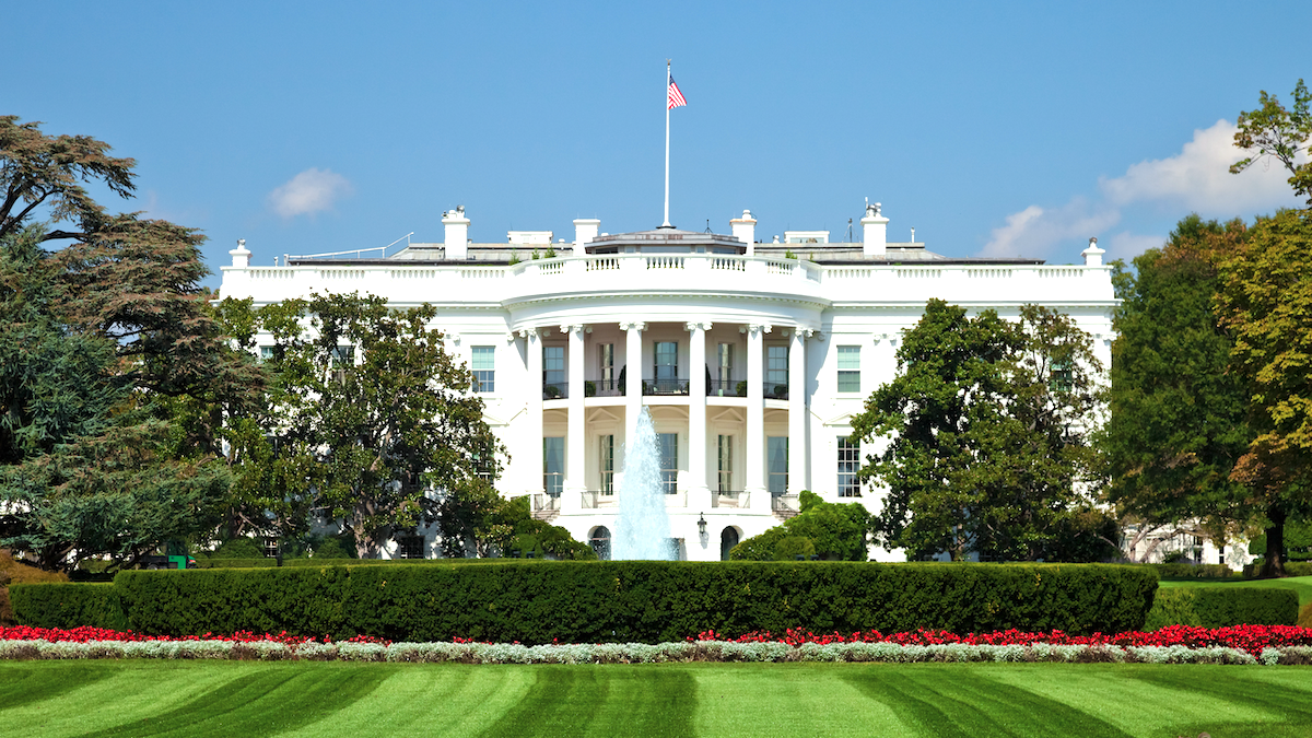 Front view of the White House with a fountain, green lawn, and the U.S. flag flying on top.