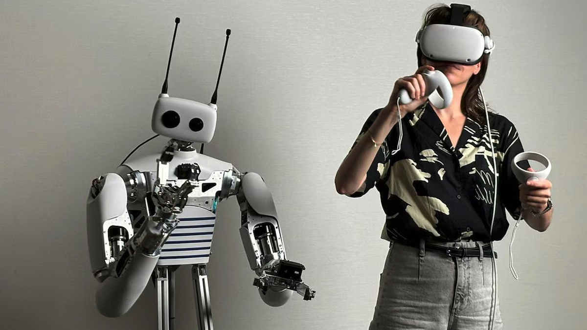 Person interacting with a humanoid robot using virtual reality headset and controllers.